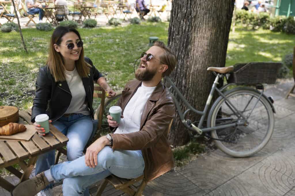 A couple wearing synthetic leather jackets having coffee and croissant in a park